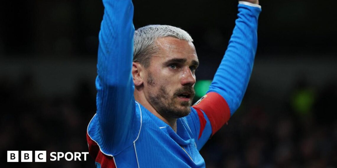 Atletico Madrid forward Antoine Griezmann, with bleached blond hair and facial hair, has both arms raised as he wears blue and red kit