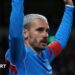 Atletico Madrid forward Antoine Griezmann, with bleached blond hair and facial hair, has both arms raised as he wears blue and red kit