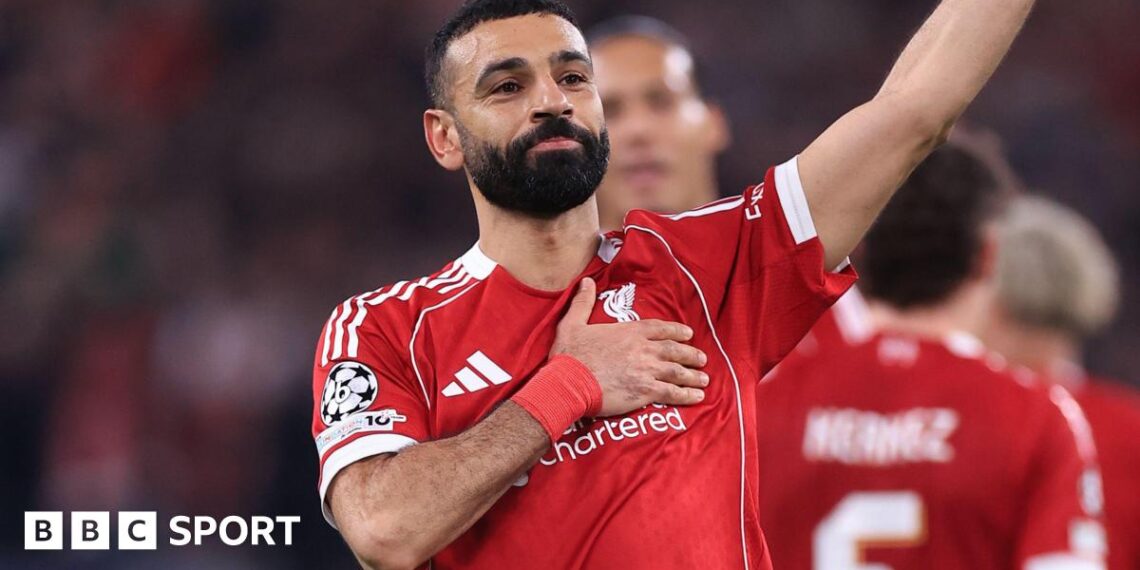 Liverpool forward Mohamed Salah waves to supporters with one hand while holding the Liverbird badge