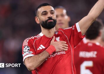 Liverpool forward Mohamed Salah waves to supporters with one hand while holding the Liverbird badge