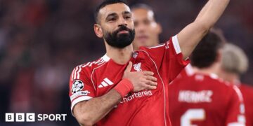 Liverpool forward Mohamed Salah waves to supporters with one hand while holding the Liverbird badge