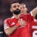 Liverpool forward Mohamed Salah waves to supporters with one hand while holding the Liverbird badge