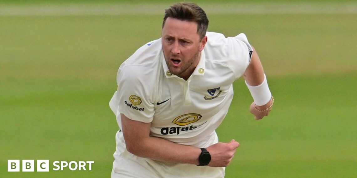 Ollie Robinson playing for Sussex and slightly hunched over with his right arm across his front and his left splayed to the back, having just completed a delivery.