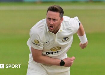 Ollie Robinson playing for Sussex and slightly hunched over with his right arm across his front and his left splayed to the back, having just completed a delivery.