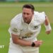 Ollie Robinson playing for Sussex and slightly hunched over with his right arm across his front and his left splayed to the back, having just completed a delivery.