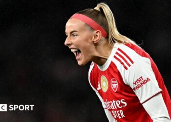 Chloe Kelly slides on her knees in celebration while wearing Arsenal's red and white kit and a red headband
