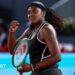 Hailey Baptiste, wearing a black vest and shorts, black headband and a ponytail, holds her green Wilson racket in her left hand and punches her right fist in celebration