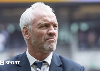 Brian McDermott, wearing a suit, looks off to the right of frame