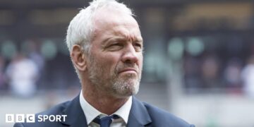 Brian McDermott, wearing a suit, looks off to the right of frame