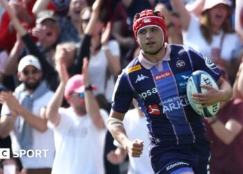 Louis Bielle-Biarrey with the ball in his left hand while wearing Bordeaux's dark and light blue striped shirt in match action
