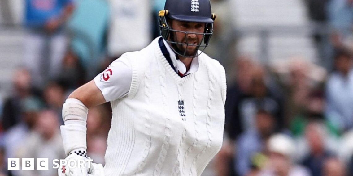 Chris Woakes grimaces with one arm in a sling and his bat in the other