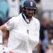 Chris Woakes grimaces with one arm in a sling and his bat in the other