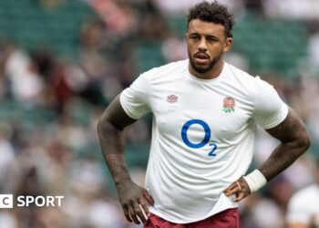 Courtney Lawes standing on the pitch with an England shirt on and his hands on his hips
