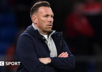 Craig Bellamy, in an open dark jacket with a grey top underneath, looks on with a focused stare during Wales' match against Northern Ireland