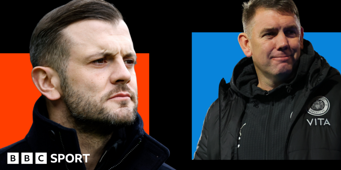 Jack Wilshere, wearing a black coat with a high collar, looks on with a serious face (left). Dave Challinor, wearing a black jacket with a Stockport county badge on, smiles (right).