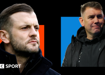 Jack Wilshere, wearing a black coat with a high collar, looks on with a serious face (left). Dave Challinor, wearing a black jacket with a Stockport county badge on, smiles (right).
