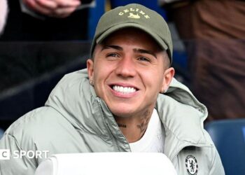 Enzo Fernandez smiling while in sat down in a Chelsea jacket