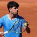 Carlos Alcaraz is wearing a blue t-shirt and holding a tennis ball to his racquet
