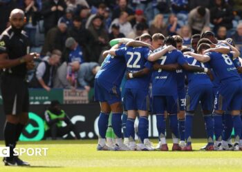 Gary Rowett, wearing a black tracksuit with Leicester branding, looks dejected on the pitch after a defeat