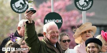 Willie Mullins smiling and holding a trophy in the air