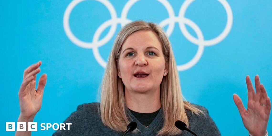 IOC president Kirsty Coventry speaking at the Winter Olympics against a background of the Olympic rings.