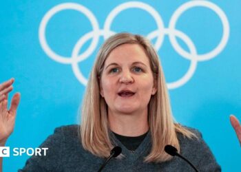 IOC president Kirsty Coventry speaking at the Winter Olympics against a background of the Olympic rings.
