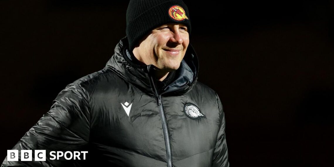 Departed Catalans Dragons head coach Joel Tomkins in club emblazoned hat and coat