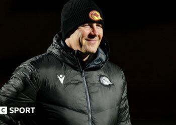 Departed Catalans Dragons head coach Joel Tomkins in club emblazoned hat and coat