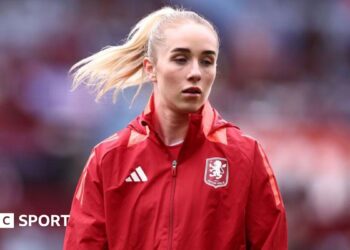 Missy Bo Kearns wearing a red jacket with an Aston Villa badge on the chest