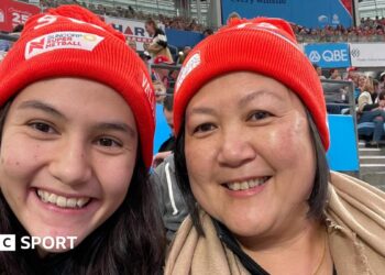 Sophie Fawns with her mother, Maureen, both smiling and wearing NSW Swifts red woolly hats