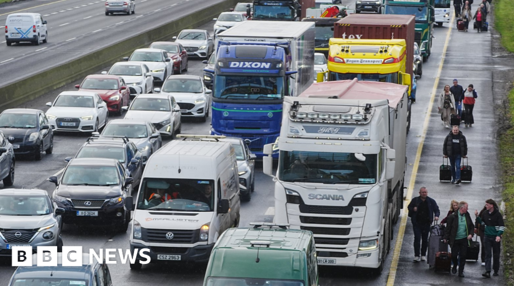 People walk with luggage past heavy traffic on Dublin's M50