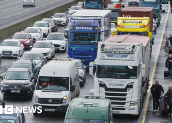 People walk with luggage past heavy traffic on Dublin's M50