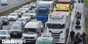 People walk with luggage past heavy traffic on Dublin's M50