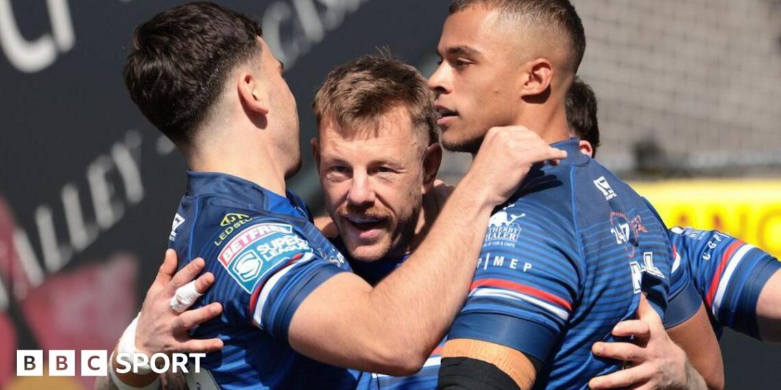 Tom Johnstone is surrounded by team-mates, all in Wakefield Trinity blue, as they celebrate one of his three tries against Bradford Bulls.