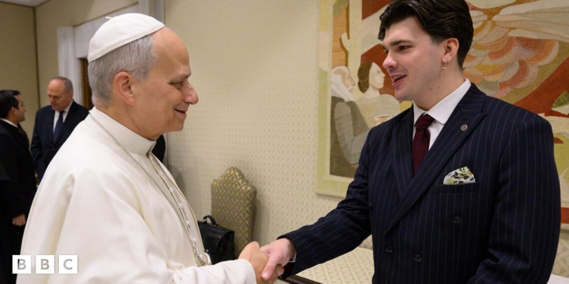 The Pope, wearing white shakes hands with Harry Clark, who is wearing a black suit.