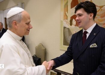 The Pope, wearing white shakes hands with Harry Clark, who is wearing a black suit.