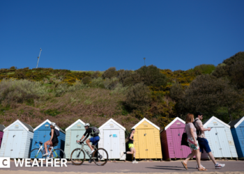 People make their way past beach huts on Bournemouth beach in Dorset.