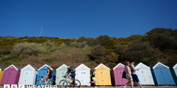 People make their way past beach huts on Bournemouth beach in Dorset.