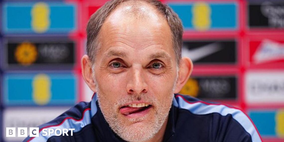 Head and shoulders view of England head coach Thomas Tuchel at a news conference, with his tongue poking out of his mouth