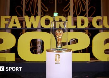 The World Cup on display on a white stand prior to the draw in December in Washington with Fifa World Cup 2026 in big gold letters in the background.