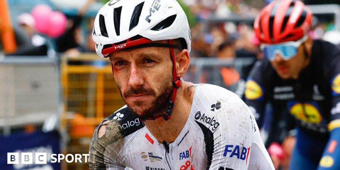 Adam Yates in a torn cycling kit and helmet, both predominantly white