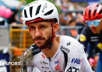 Adam Yates in a torn cycling kit and helmet, both predominantly white