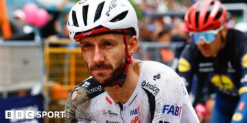 Adam Yates in a torn cycling kit and helmet, both predominantly white