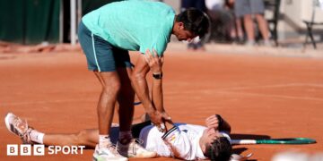 Jakub Mensik lies on the floor and opponent Mariano Navone tries to assist him