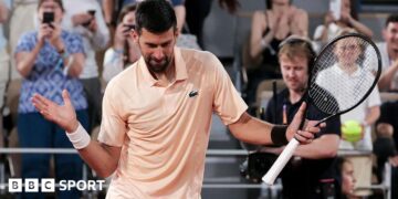 Novak Djokovic, wearing a peach polo shirt, dances with his racquet in his left hand