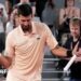Novak Djokovic, wearing a peach polo shirt, dances with his racquet in his left hand
