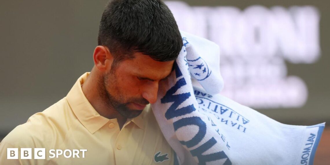 Novak Djokovic reacts during the Italian Open, raising a towel to his face while wearing a yellow tennis shirt