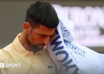 Novak Djokovic reacts during the Italian Open, raising a towel to his face while wearing a yellow tennis shirt