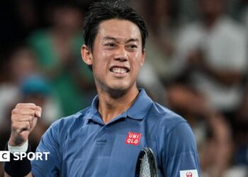 Japan player Kei Nishikori, in a blue polo shirt, pumps his fist on a tennis court, blurred crowd behind him