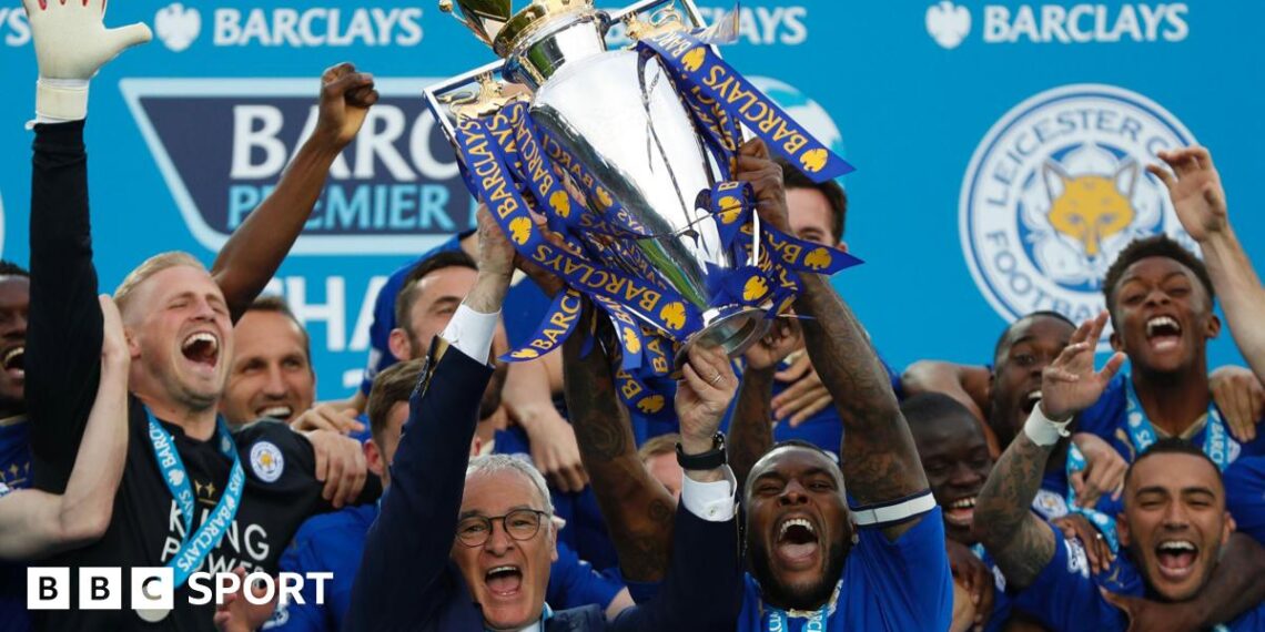 Leicester City manager Claudio Ranieri and captain Wes Morgan lift the Premier League trophy while surrounded by euphoric Foxes players